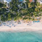 Vista aérea de la playa de Dominicus Bayahíbe con palmeras, arena blanca, reposeras y mar turquesa en la costa sureste de República Dominicana.