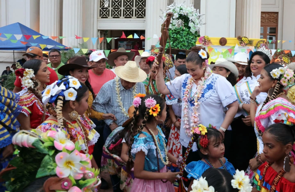 La alcaldesa de Managua, Reyna Rueda, rodeada de tradicionalistas y niñas con trajes folklóricos nicaragüenses, sostiene la Tajona durante la ceremonia oficial de las fiestas en honor a Santo Domingo de Guzmán frente al Palacio Municipal.