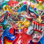 Primer plano vibrante de varios Diablos Cojuelos dominicanos luciendo máscaras coloridas de rasgos exagerados, dientes afilados y cuernos, decoradas con lentejuelas y plumas durante el Desfile Nacional de Carnaval.