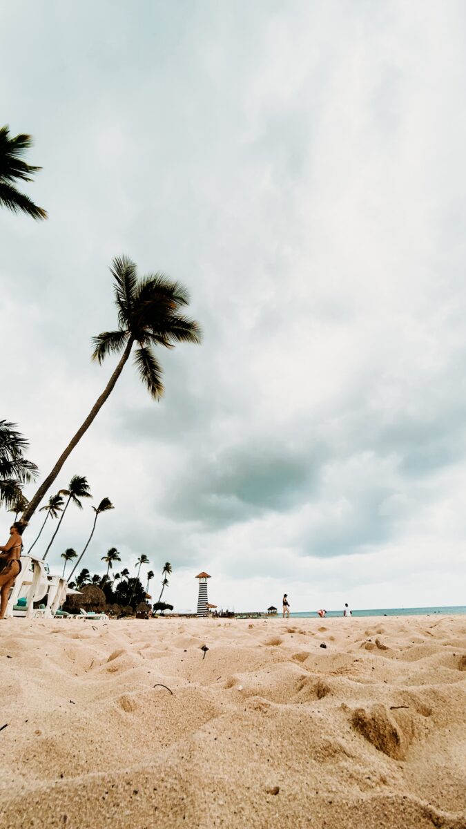 Playa de arena clara en Bayahíbe, República Dominicana, con palmeras, mar Caribe y cielo nublado.